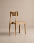 The Noki Dining Chair | Wood by Wooden Stories, featuring a curved backrest and clean, minimalist design in solid wood, is set against a neutral beige background with its back facing the viewer.