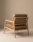 The Nysse Lounge Chair | Leather by Wooden Stories features clean, modern Scandinavian lines, a light wooden frame, and tan leather cushions. It’s shown angled against a beige background for a minimalist look.