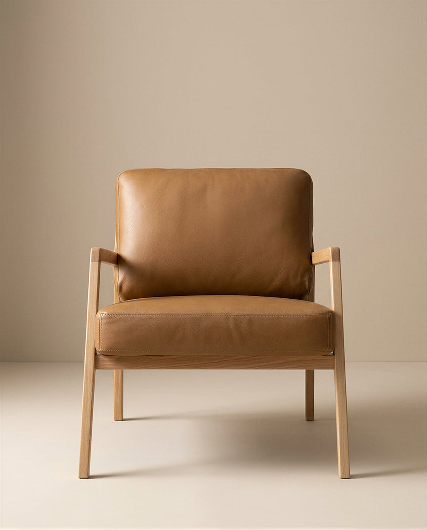The Nysse Lounge Chair by Wooden Stories showcases modern Scandinavian style, with light wooden legs and frame, plus tan leather cushioned seat and backrest, set against a plain beige background.