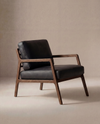 The Wooden Stories Nysse Lounge Chair | Leather features a dark wooden frame and black leather cushions, showcasing a minimalist Scandinavian design with clean lines, set against a neutral beige background.
