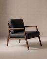 The Wooden Stories Nysse Lounge Chair | Leather features a dark wooden frame and black leather cushions, showcasing a minimalist Scandinavian design with clean lines, set against a neutral beige background.