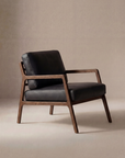 The Wooden Stories Nysse Lounge Chair | Leather features a dark wooden frame and black leather cushions, showcasing a minimalist Scandinavian design with clean lines, set against a neutral beige background.