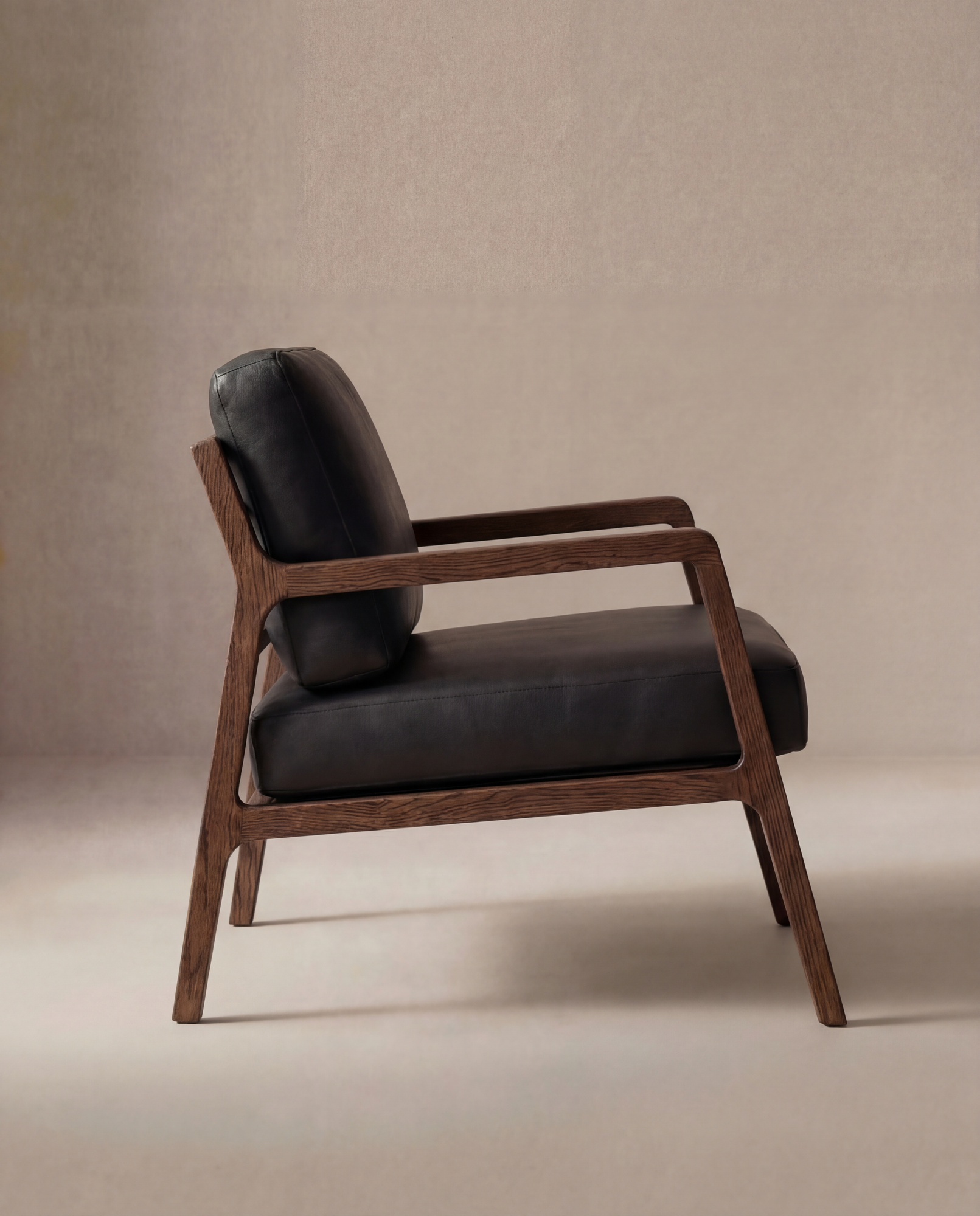 A side view of the Wooden Stories Nysse Lounge Chair | Leather showcases its Scandinavian design with a solid oak frame and black leather seat and backrest, set against a neutral beige background.