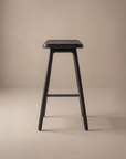 The Odd Counter Stool by Wooden Stories, crafted from solid oak with four legs and a rectangular seat, stands on a neutral beige background, highlighting timeless minimalist design.