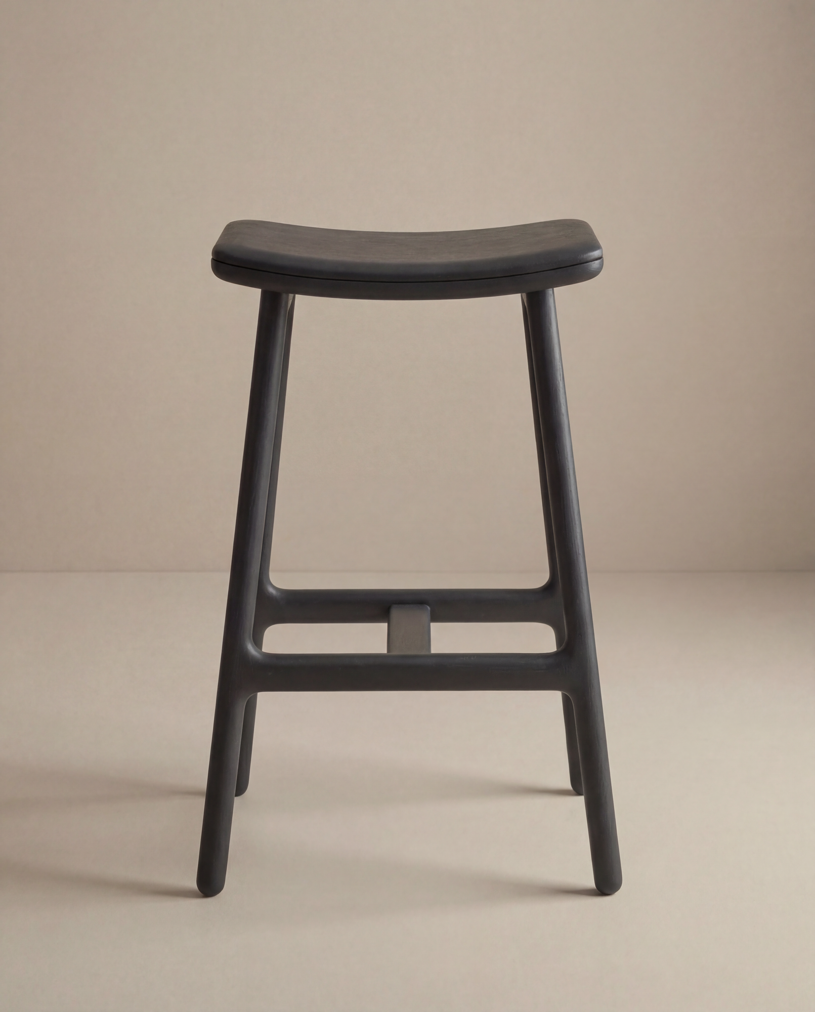 The Odd Counter Stool | Leather by Wooden Stories features four legs and a gently curved seat, shown here against a plain beige background.