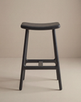 The Odd Counter Stool | Leather by Wooden Stories features four legs and a gently curved seat, shown here against a plain beige background.