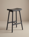 The Odd Counter Stool | Leather by Wooden Stories features a modern design with a curved leather seat and four legs, ideal for kitchen island seating, showcased against a neutral beige background.