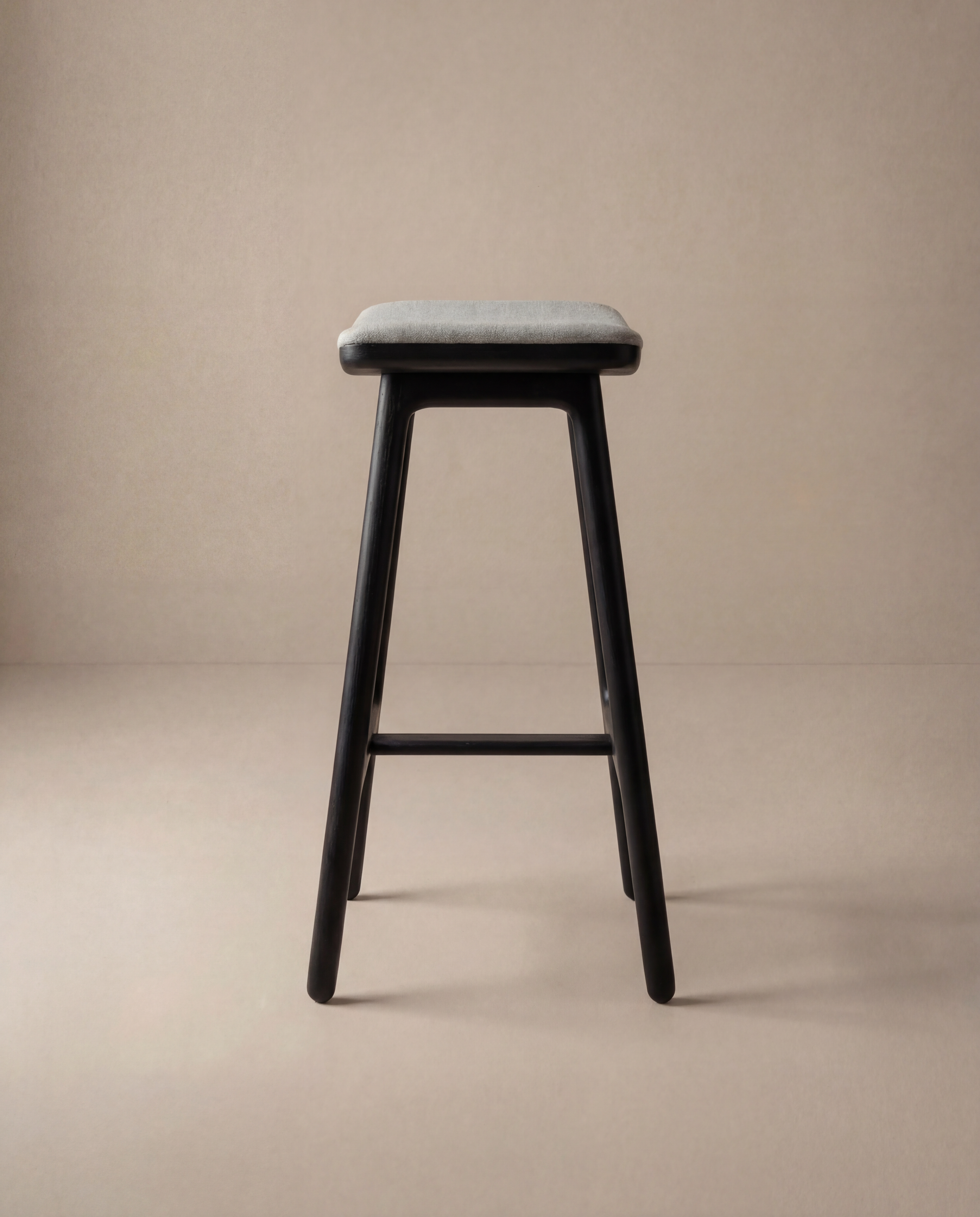 The Odd Counter Stool | Fabric by Wooden Stories features a rectangular gray cushioned seat with black wooden legs, inspired by Danish design and shown against a plain beige background.
