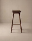 The Odd Counter Stool | Wood by Wooden Stories is a simple solid oak stool with four legs, a rectangular seat, and footrest, shown against a neutral beige background—timeless furniture for any space.