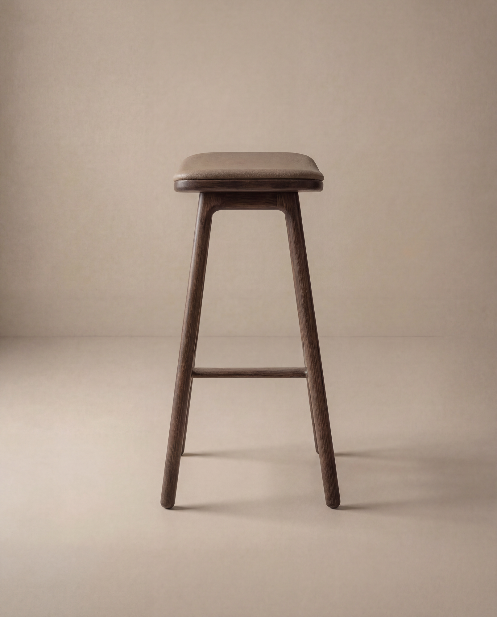 The Odd Counter Stool | Leather by Wooden Stories features a minimalist design with a rectangular seat and four angled legs, showcased against a plain beige background.