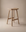 The Odd Counter Stool | Wood by Wooden Stories is a minimalist solid oak stool with a curved seat, four legs, and visible natural wood grain, shown against a neutral beige background. Its simple, modern design makes it perfect for any space.