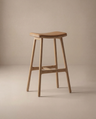 The Odd Counter Stool | Leather by Wooden Stories features a minimalist, modern design with a curved seat, four straight legs, and a natural wood finish—ideal as kitchen island seating and shown against a neutral beige background.