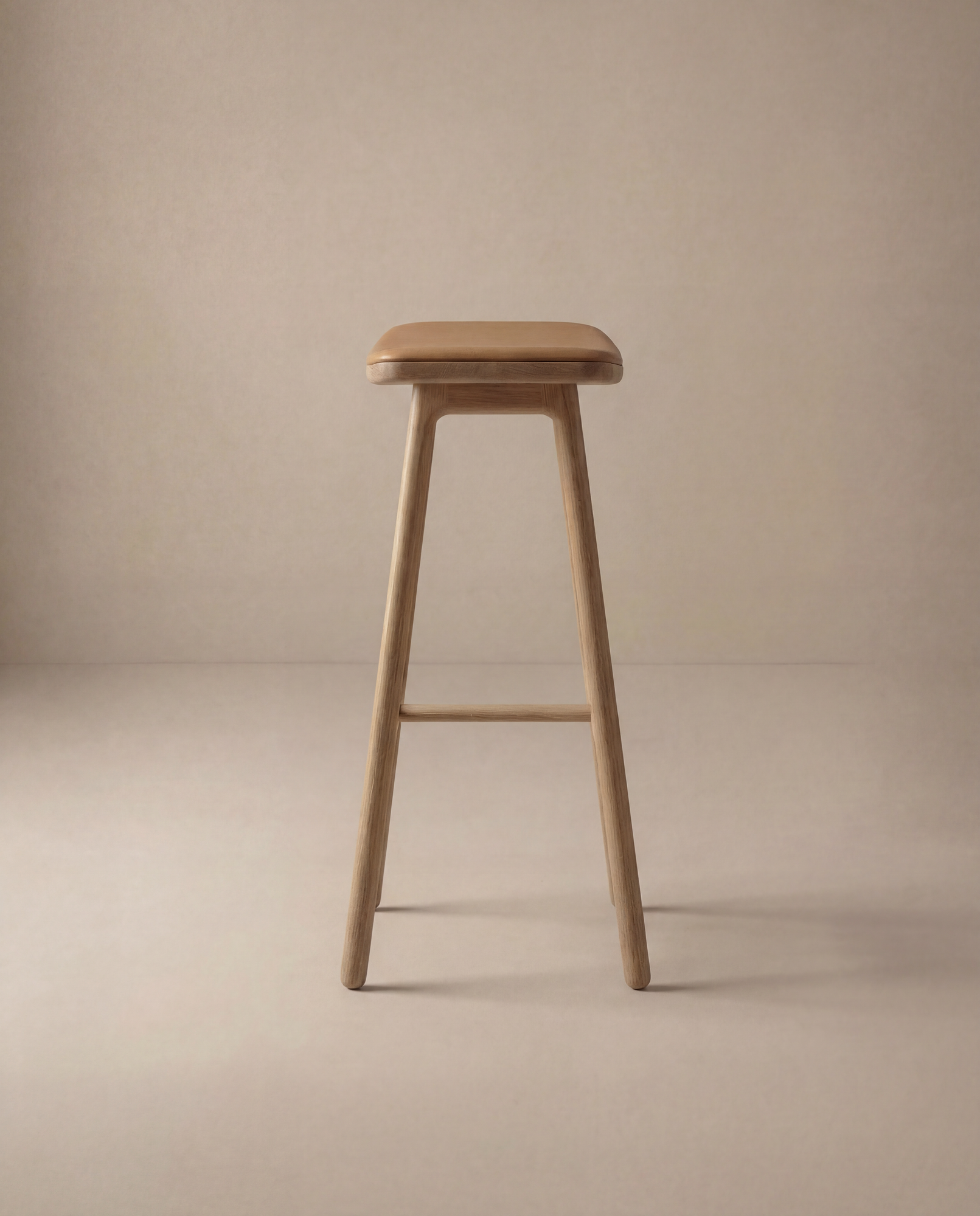 The Odd Counter Stool | Leather by Wooden Stories features a minimalist solid oak frame with a brown leather cushioned seat, shown on a light beige background—ideal for stylish and sturdy kitchen island seating.