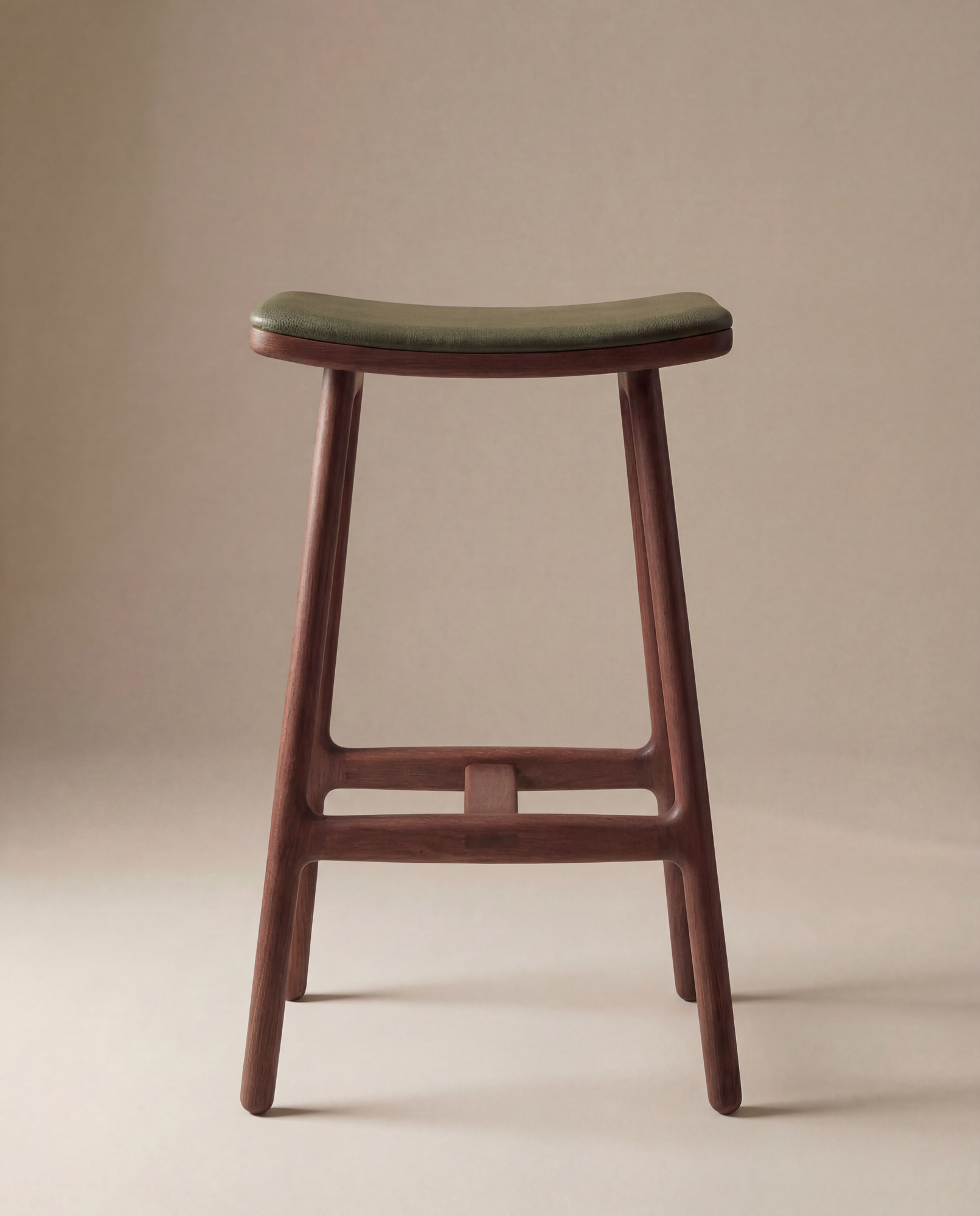 The Odd Counter Stool | Leather by Wooden Stories features four solid oak legs, a curved seat, and green Italian leather upholstery, shown on a neutral beige background.