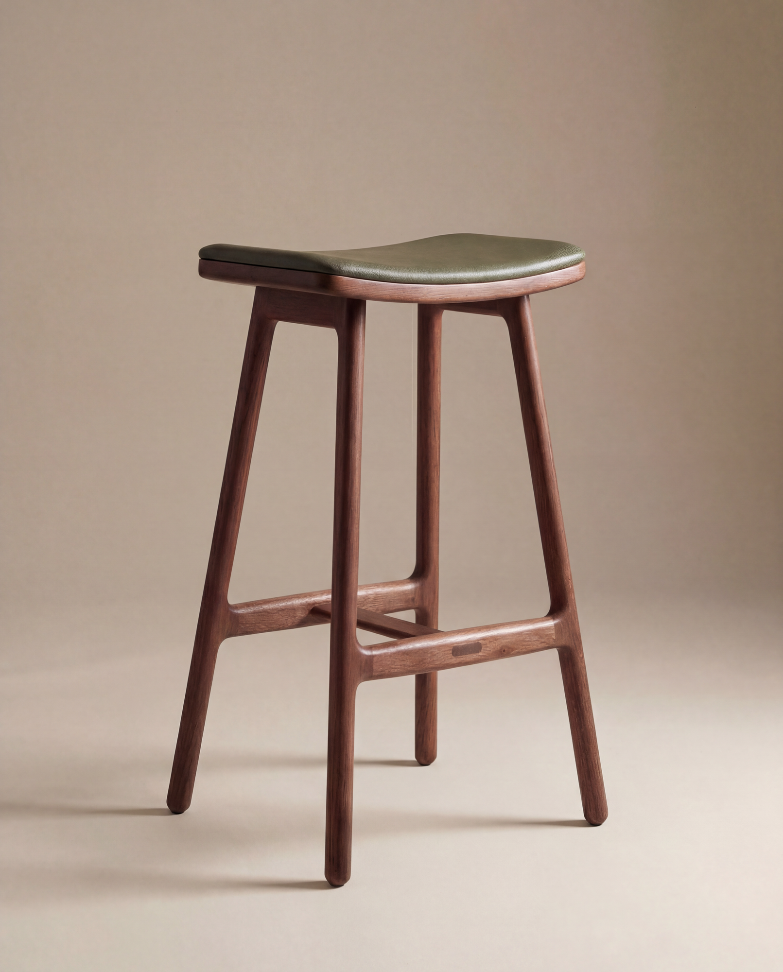 The Odd Counter Stool | Leather by Wooden Stories features a minimalist solid oak frame, dark green curved leather seat, and four angled legs—ideal for stylish kitchen island seating against a neutral beige backdrop.