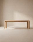 The Oli Dining Table by Wooden Stories, a minimalist Danish design with rounded edges and four legs, is shown against a neutral beige background in soft, natural light.