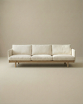 The Pensive Sofa | Fabric by Wooden Stories is a modern, minimalist Danish cream sofa with three seat cushions and wooden legs, shown against a plain beige background.
