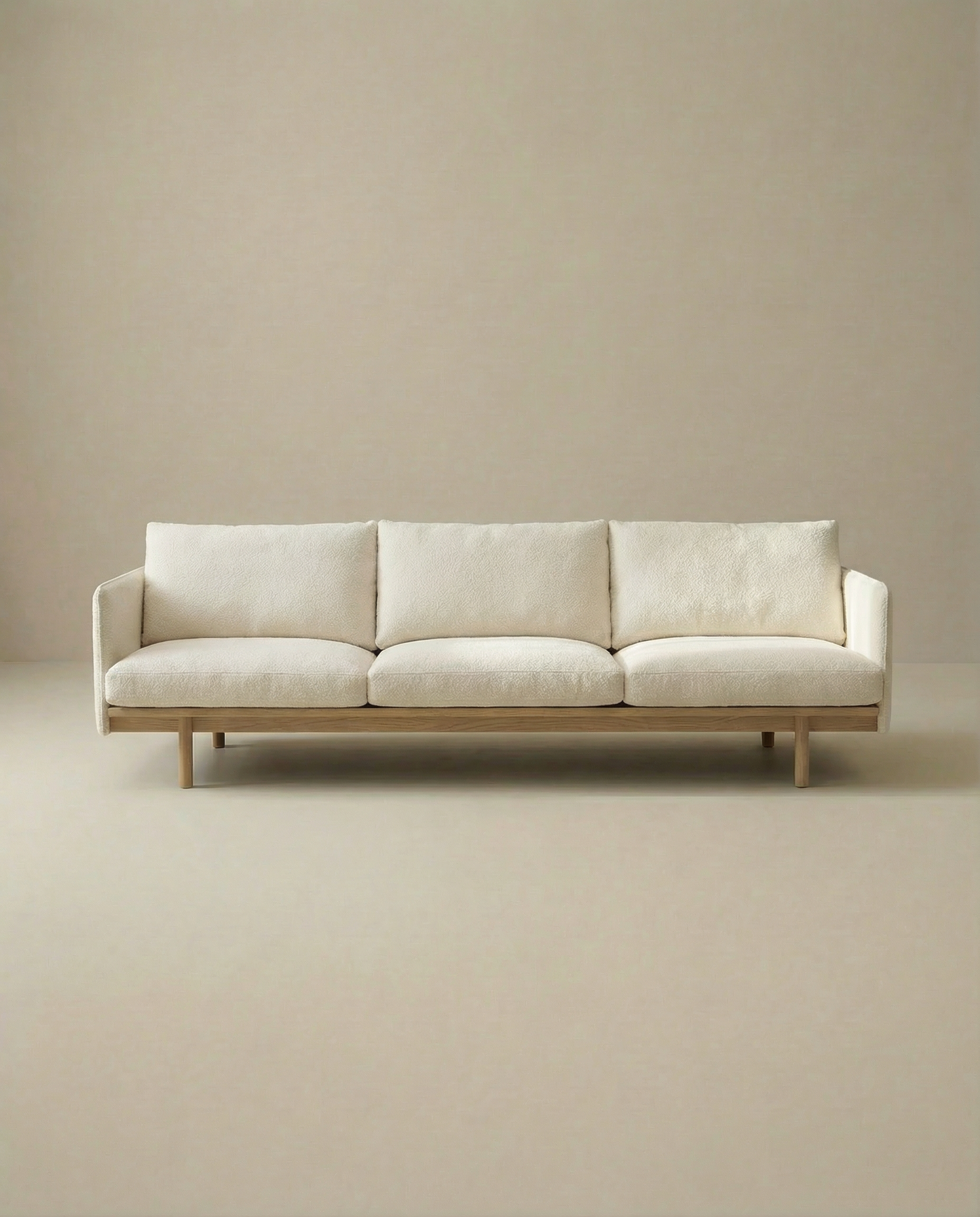 The Pensive Sofa | Fabric by Wooden Stories is a modern, minimalist Danish cream sofa with three seat cushions and wooden legs, shown against a plain beige background.