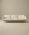 The Pensive Sofa | Fabric by Wooden Stories is a modern, minimalist Danish cream sofa with three seat cushions and wooden legs, shown against a plain beige background.