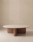 The Pivot Coffee Table | Round - Wood & Stone by Wooden Stories features a smooth, light stone top and intersecting solid oak base, presented against a plain beige background.