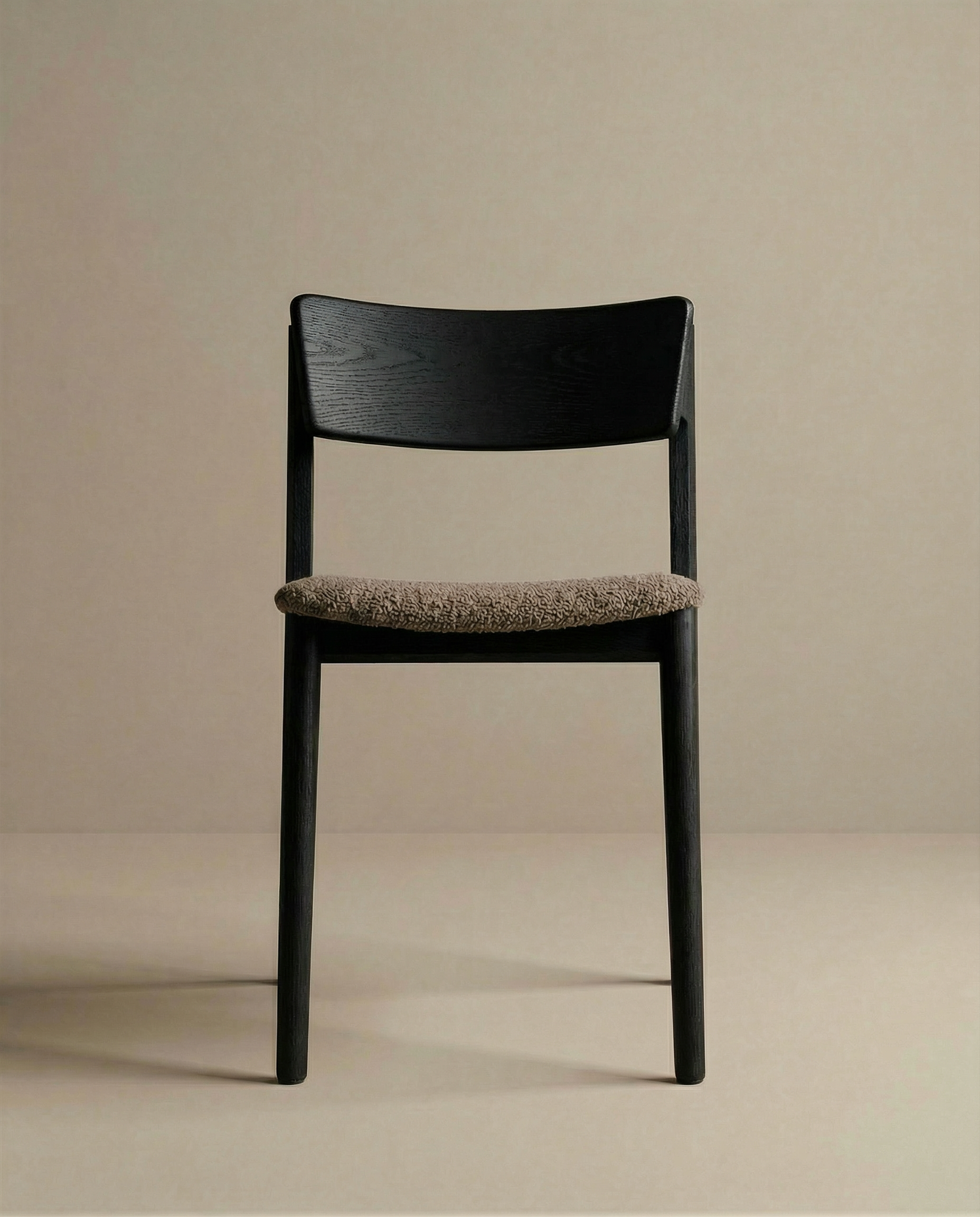 The Poise Dining Chair by Wooden Stories features a minimalist black oak frame and textured light brown fabric seat, centered against a plain beige background and facing the camera.