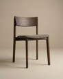The Poise Dining Chair by Wooden Stories features an espresso oak frame, curved backrest, four legs, and a cushioned gray fabric seat, shown against a plain beige background.
