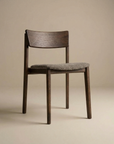 The Poise Dining Chair by Wooden Stories features an espresso oak frame, curved backrest, four legs, and a cushioned gray fabric seat, shown against a plain beige background.