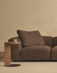 A modern living room with a brown fabric sofa, a beige carpet, a light brick wall from the Danish Collection, and a solid oak Wooden Stories Guild Side Table holding a cup.