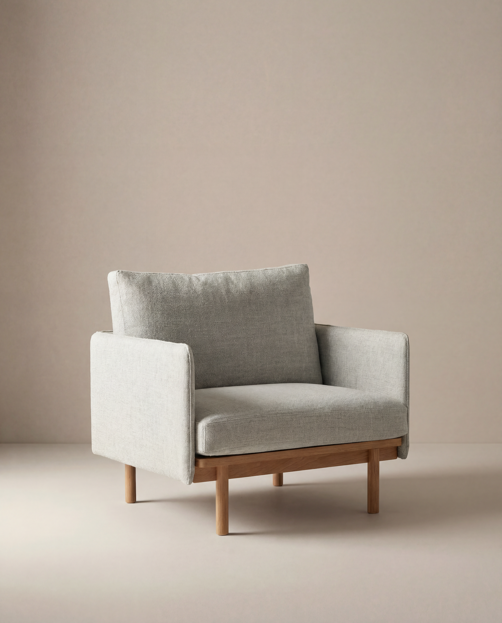 The Pensive Lounge Chair | Fabric by Wooden Stories features light grey upholstery, a wooden base, and clean mid-century lines, creating a simple, contemporary look in a minimalist room with neutral beige walls and floor.