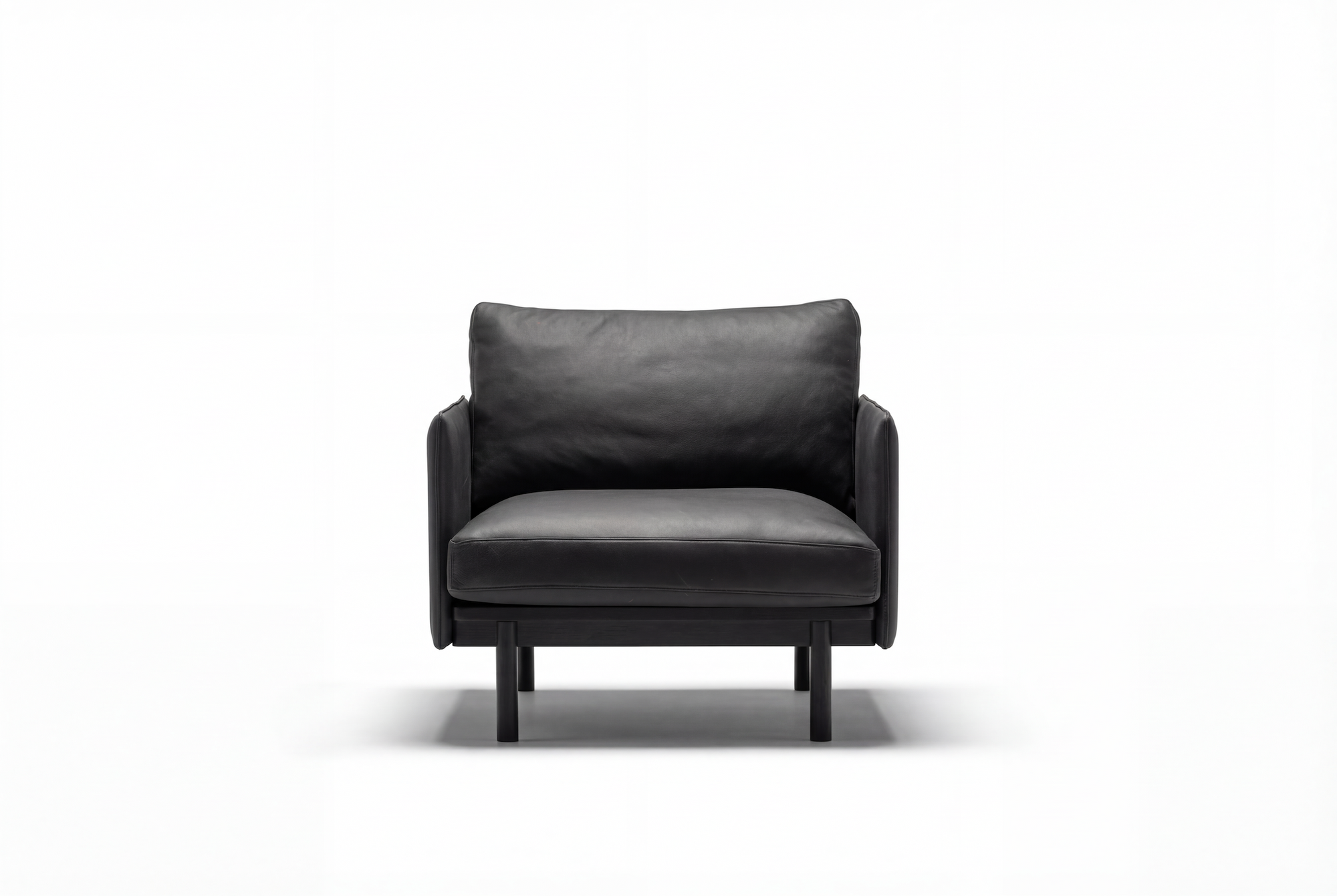 The Pensive Lounge Chair | Leather by Wooden Stories is a modern black leather armchair with Danish-inspired lines, cushioned seat and backrest, wooden legs, and a minimalist design, shown against a plain white background.