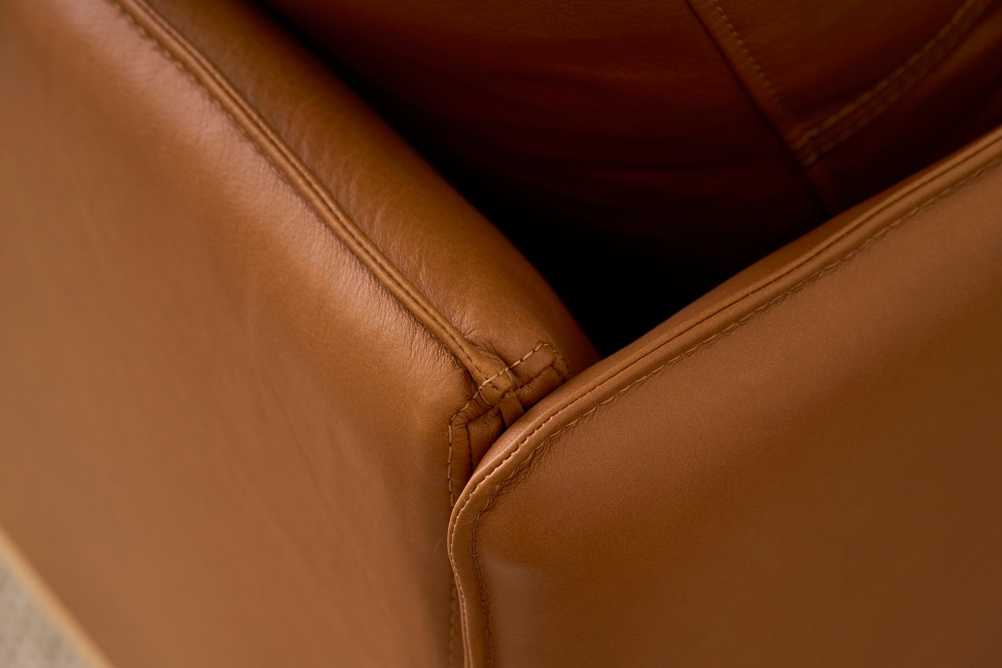 Close-up of the corner and seams of the Pensive Sofa | Leather by Wooden Stories, showcasing detailed stitching and the rich texture of its brown leather upholstery.