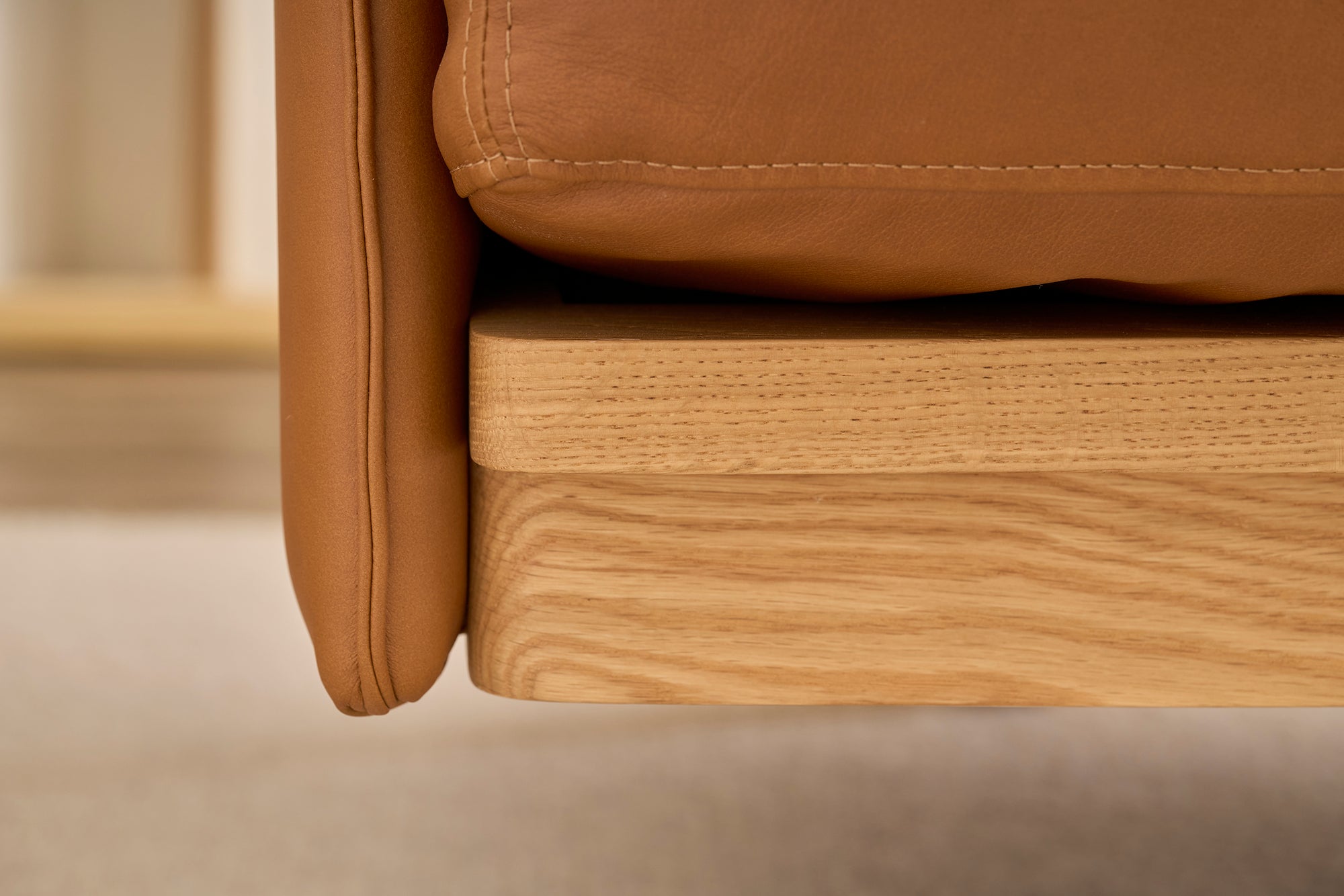 Close-up of the Pensive Sofa | Leather by Wooden Stories, featuring a tan leather cushion on a light wood frame and showcasing the detailed textures of both premium leather and fine Danish craftsmanship.