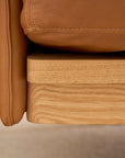 Close-up of the Pensive Sofa | Leather by Wooden Stories, featuring a tan leather cushion on a light wood frame and showcasing the detailed textures of both premium leather and fine Danish craftsmanship.
