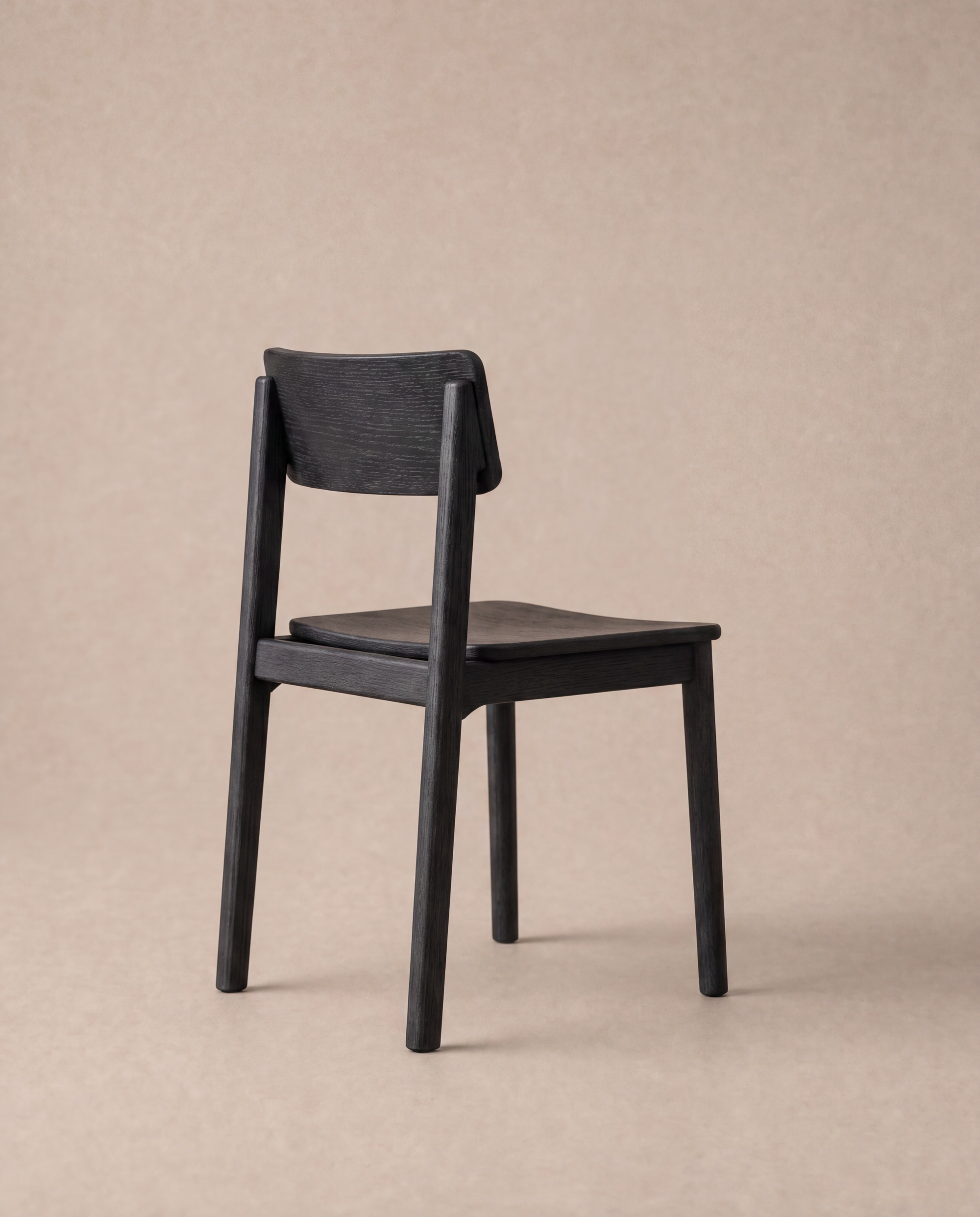 The Poise Dining Chair | Wood by Wooden Stories, featuring a simple modern design in dark solid oak from the Danish Collection, is positioned on a light beige background, angled slightly away to display its backrest and seat.