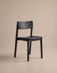 A Poise Dining Chair | Wood by Wooden Stories, crafted with solid oak in a sleek black finish and minimalist design, is showcased against a neutral beige background.