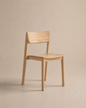 The Poise Dining Chair | Wood by Wooden Stories, featuring a minimalist solid oak design with a straight backrest and no armrests from the Danish Collection, is displayed on a neutral beige background.