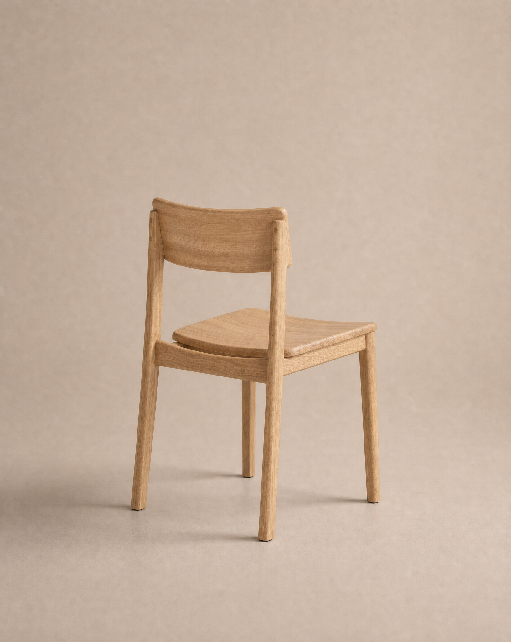 A minimalist solid oak Poise Dining Chair from Wooden Stories’ Danish Collection, featuring a curved backrest and no armrests, positioned at an angle on a plain beige background.