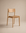 The Poise Dining Chair | Leather by Wooden Stories features a minimalist solid oak frame with a curved backrest and a flat leather seat, presented against a neutral beige background.
