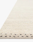 Close-up side view of the Sloane Rug - Mist by Loloi, a hand-woven, off-white rug featuring a textured finish and subtle black stitch accents along the edge. This contemporary bohemian piece from the Sloane Collection is displayed on a white background.