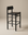 The Cesco Counter Stool by SOBU features a modern black finish in solid American ash, paired with a flat top grain leather seat, a low rectangular backrest, and simple straight legs. It is set against a plain beige background.