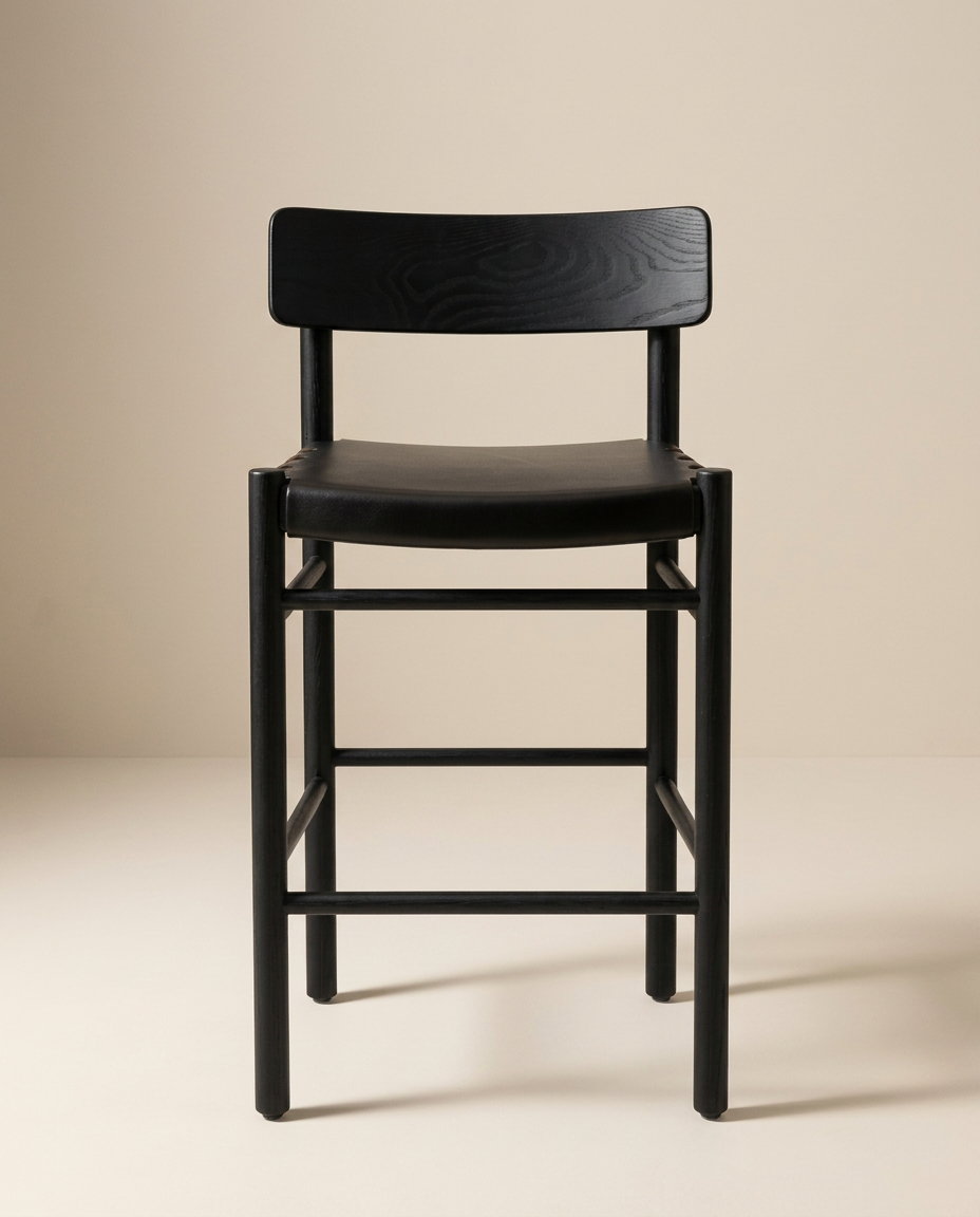 The Cesco Counter Stool by SOBU features a modern design in black ash, with a rectangular backrest, a flat top grain leather seat, and straight legs crafted from solid American ash. It is photographed against a plain beige background.