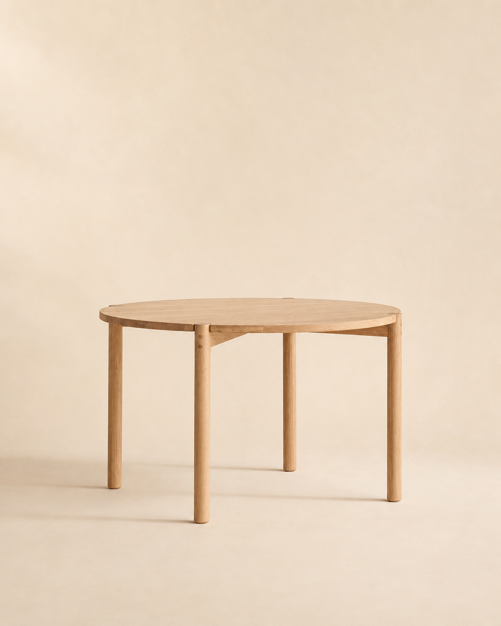 The Cove Dining Table | Light Oak by Wooden Stories features a simple, round design expertly crafted from solid American oak, supported by four sturdy legs. Showcased against a neutral beige background, its contract-grade construction offers lasting style and durability.
