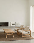 Minimalist living room with two beige armchairs, a SOBU Mars Live Edge Coffee Table - White Ash, a neutral rug, and built-in fireplace. A framed photo and white lamp sit on the mantel; light streams through tall curtains.