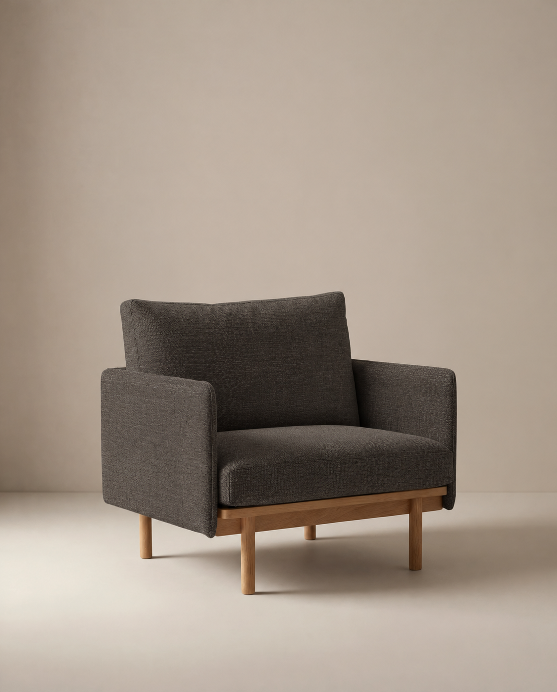 The Pensive Lounge Chair | Fabric by Wooden Stories, featuring dark gray upholstery and wooden legs with Danish-inspired design, sits against a plain, light background.