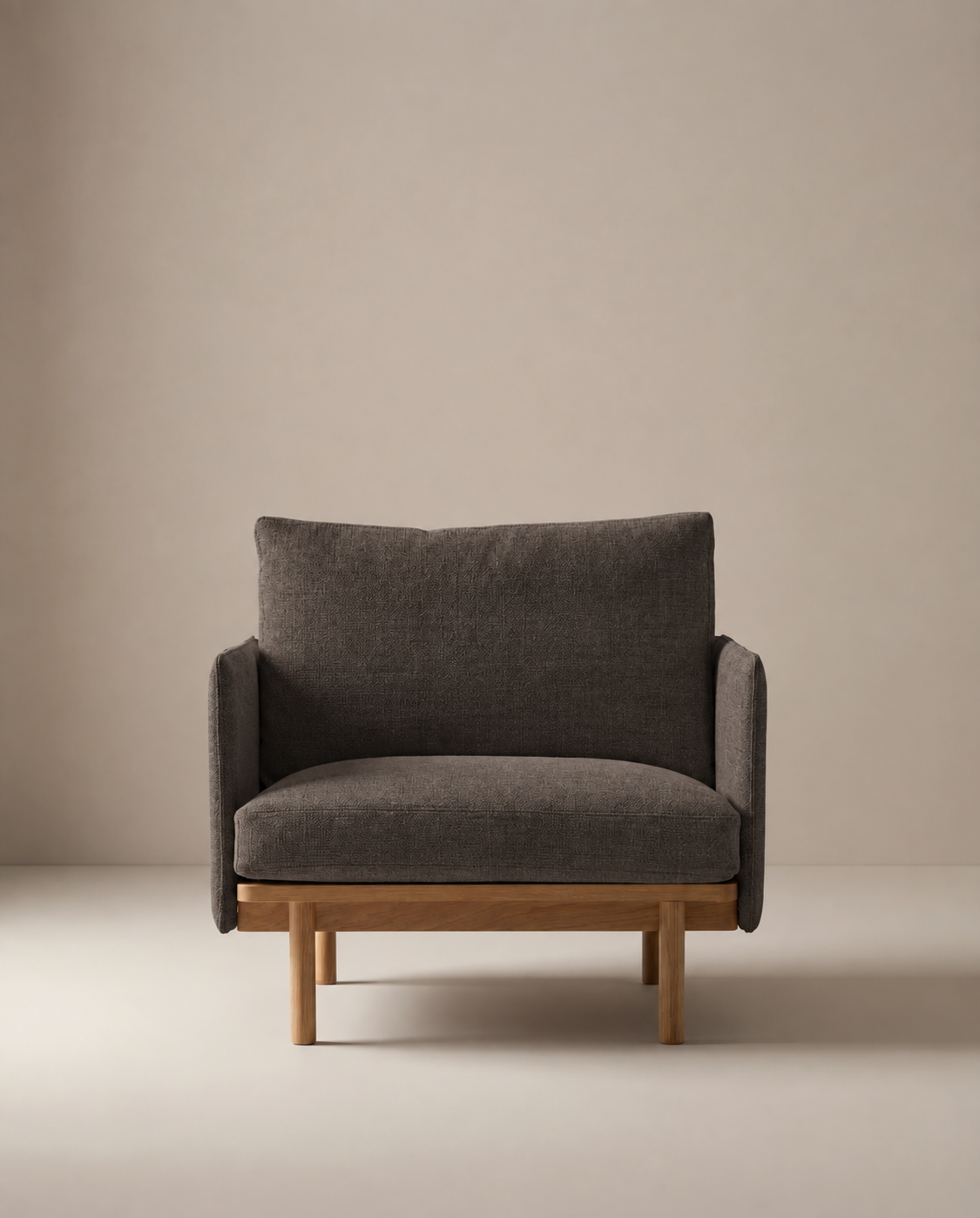 The Pensive Lounge Chair | Fabric by Wooden Stories features dark gray upholstery and a wooden frame with mid-century Danish inspiration, showcased against a plain light beige background.