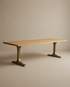 The SOBU Tommaso Dining Table features a rectangular solid wood top and two wide, curved brass T-leg pedestals, set against a plain beige background.