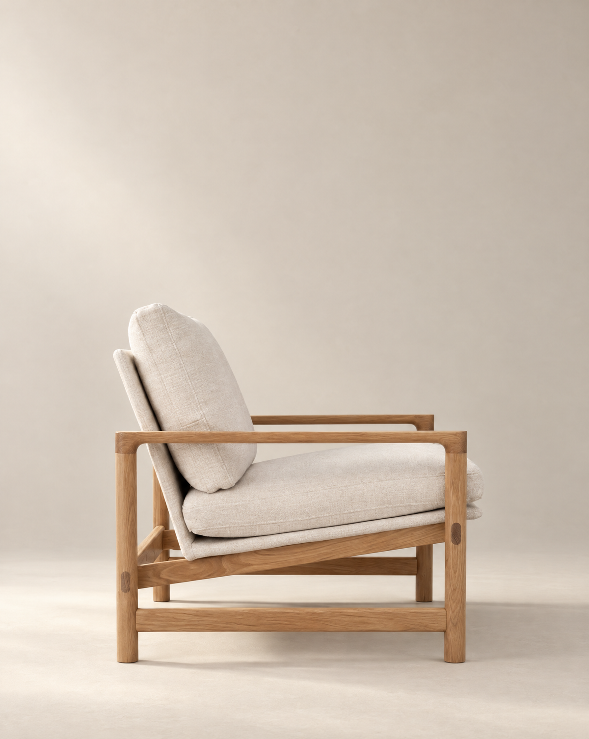 The Troubadour Lounge Chair | Fabric by Wooden Stories features a wooden frame and light beige cushions, shown in profile against a neutral backdrop to highlight its modern, mid-century-inspired design.