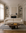 A modern living room featuring a cream Baker Sofa by Wooden Stories in fabric, paired with an abstract coffee table, striped rug, built-in shelves adorned with decorative objects, and a large framed blank artwork above a classic fireplace. Natural light streams through sheer curtains.