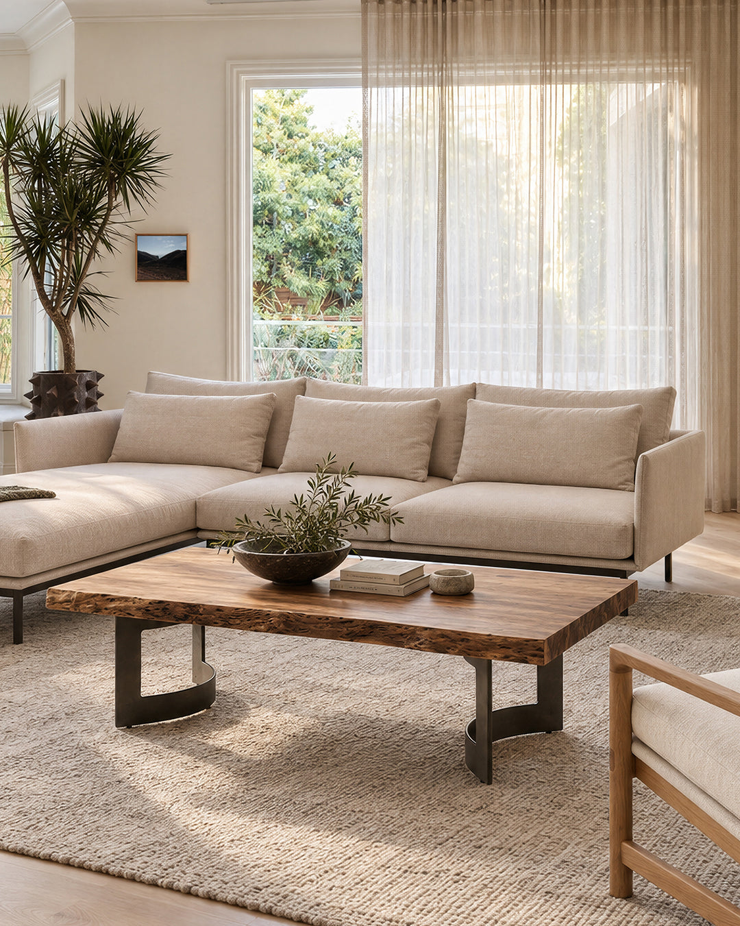 A Moes Leviathan Live Edge Coffee Table with curved black metal legs sits on a rug in front of a neutral-colored sectional sofa.