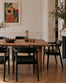 Sven Dining Chair - Black Ash with a curved backrest and a solid seat, positioned around a wooden table in a room with a fireplace.